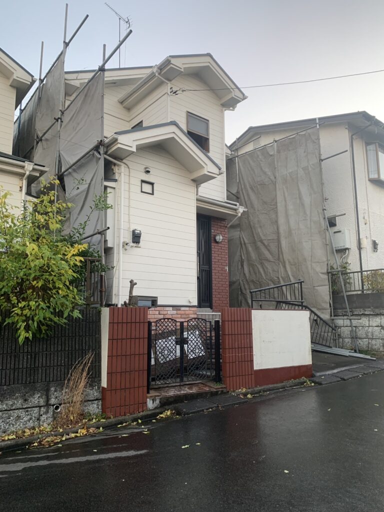 白い一戸建ての周りに養生シートがついた写真。